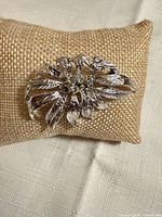 Front view of silver-tone leaf brooch showing rhinestone centre and textured leaves