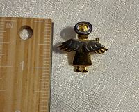 Front view of gold-tone angel brooch beside ruler showing ~1 inch height