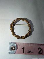 Front view of gold-tone circular brooch with measuring tape indicating size