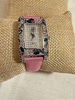 Front view of watch on display pillow showing crystal-covered dial and bezel with colored accents