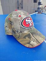 Front left view of camouflage cap showing team logo and curved brim