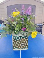 Full view of artificial flower arrangement in white metal lattice planter on table