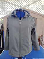Front view of sage green hooded rain jacket on mannequin