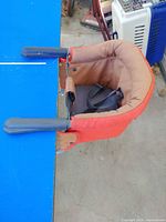 Top view of clamp-on toddler booster seat attached to tabletop showing clamps, seat fabric, and harness