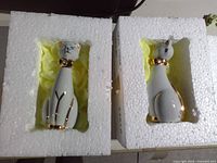 Two porcelain cat figurines inside Styrofoam inserts