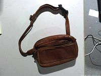 Front view of brown leather fanny pack showing both zippered compartments and strap