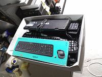 Top view of cardboard box showing several black wired keyboards and a turquoise Logitech keyboard-mouse combo box