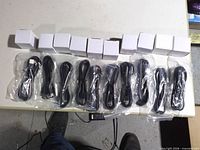Ten USB-C cables in plastic sleeves and ten white adapter boxes laid out