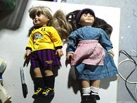Both dolls full view on table showing outfits and footwear