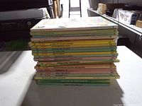 Side view of stacked pastel-spine hardcover children’s books showing quantity and varied titles