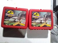 Two red Jurassic Park lunchboxes front graphics visible