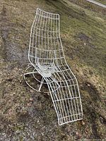 Side view of white wire-frame swivel chaise lounge on grass