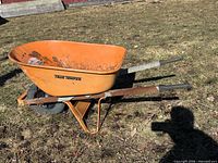 Left side view of orange True Temper wheelbarrow on grass