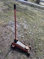 Full view of red hydraulic floor jack standing on ground