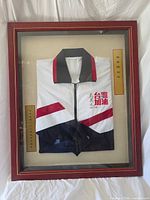 Full view of framed windbreaker showing logo, signature, plaques and frame