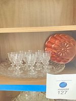 Two glass platters overlapped with ten cordial glasses arranged on top; brass fluted mold leaning at back