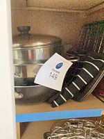 Cabinet shelf with stainless stock pot, pasta insert, black striped apron, muffin pans, baking sheets, wire racks