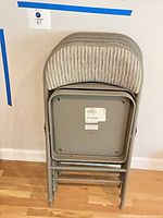 Stack of four gray metal folding chairs folded against wall