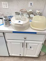 All items grouped on countertop: Tupperware pieces, glass jars, Microbuddy set, aluminum milk frother