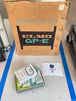 Front of Elmo GP-E 8mm Projector cardboard box with playing cards in foreground