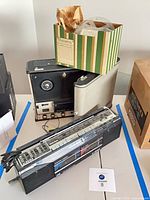 Sony reel-to-reel recorder, JVC boombox, two tape reels in striped box visible together