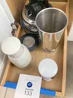 Drawer showing stainless blender jar, two white manual choppers, black blade assembly