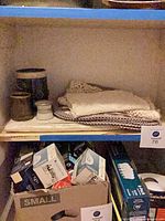 Shelf showing lace linens stacked beside three ceramic vessels