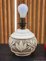 Front view of chalkware lamp with bulb installed showing floral relief and socket