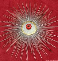 Frontal view on red background showing complete starburst with rear mounting cap and gilt rim