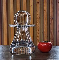 Full view of clear crystal decanter beside red object for scale