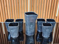 Front view of pitcher flanked by six matching cups on reflective surface