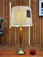 Front view of lamp showcasing wood column, brass base, and linen shade