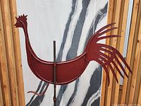 Side view of red metal rooster silhouette on rod showing tail detail
