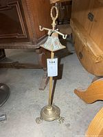 Full view of brass fireplace tool holder showing top handle, three-arm rest, and paw-footed base