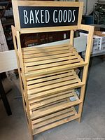Front view of wooden rack showing five slat shelves and BAKED GOODS sign
