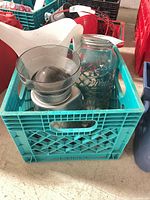 Green milk crate containing coffee grinder with hopper, large Mason jar, and white jug