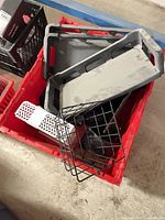 Overview of items inside red crate: two grey plastic trays, black wire basket, and other contents