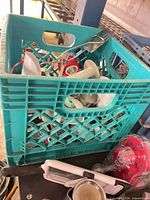 Overall view of green milk crate and assorted utensils inside and around it