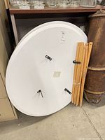 White round tabletop leaning with bundled wood legs and brackets visible