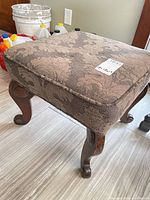 Full view of foot stool showing carved legs and upholstery