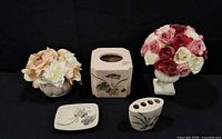 Five ceramic bathroom decor items arranged on black background: tissue box cover, toothbrush holder, soap dish, two vases with artificial flowers
