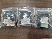 Front view of three resin building miniatures in sealed bags