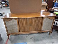 Front view of wood console stereo cabinet with cloth speaker panels and central tambour doors
