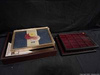 Group shot showing wooden case, metal-framed glass cover, and two black plastic trays with red compartments