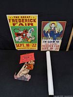 Two posters, die-cut clown sign, rolled poster on black backdrop