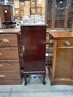 Front view of tall mahogany jewelry cabinet between other furniture