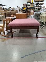 Front angle showing full ottoman with wooden legs and pink upholstery