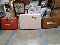 Front view of three vintage hard-shell suitcases: red, cream Samsonite, brown
