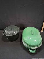 Black speckled stock pot and green roaster with lids shown together