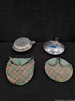 Two aluminum items and two plaid covers displayed on black backdrop